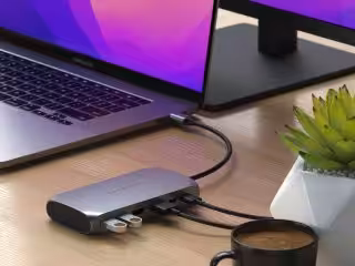 Satechi Dockingstation mit mehreren Anschlüssen, angeschlossen an einen MacBook Laptop, im modernen Arbeitsbereich mit Kaffeetasse, Pflanzen, Streaming- und Smart-Home-Geräten.