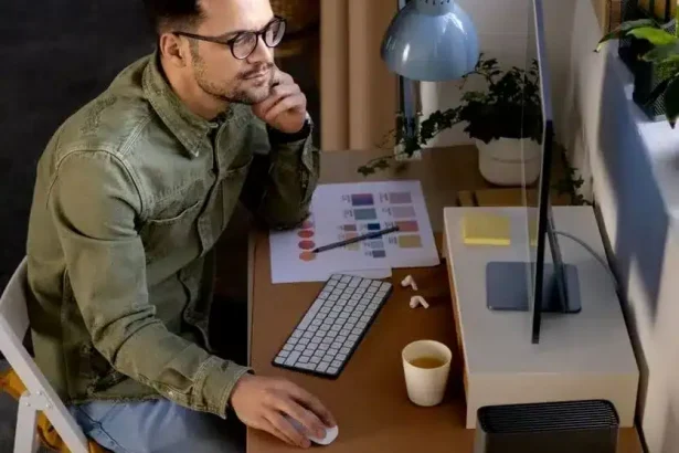 Sitzender Mann arbeitet an Smart-Home-Technologie an einem modernen Schreibtisch. Er nutzt einen Computer, eine Tastatur, eine Maus, und hat Kaffeetasse sowie Pflanzen im Umfeld.