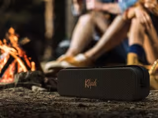 Kabelloser tragbarer Lautsprecher vor Lagerfeuer in der Natur, perfekt für Camping und Outdoor-Aktivitäten.