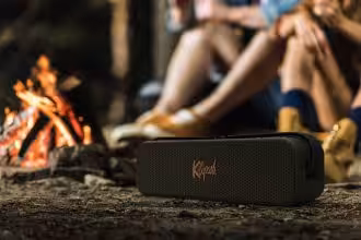 Kabelloser tragbarer Lautsprecher vor Lagerfeuer in der Natur, perfekt für Camping und Outdoor-Aktivitäten.