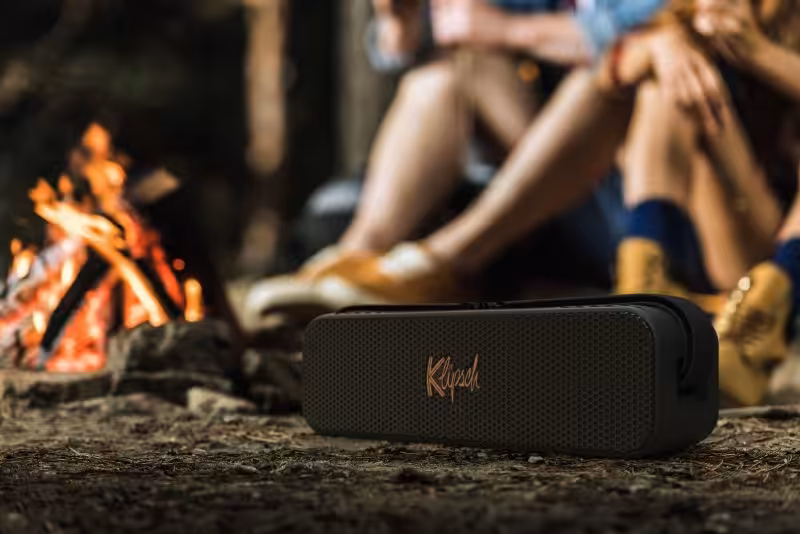 Kabelloser tragbarer Lautsprecher vor Lagerfeuer in der Natur, perfekt für Camping und Outdoor-Aktivitäten.