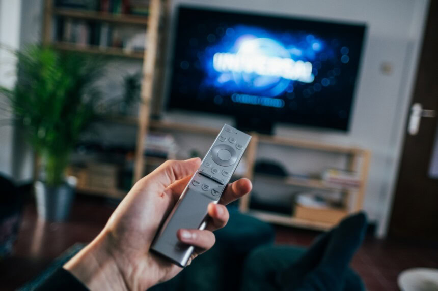 a hand holding a remote control in front of a television