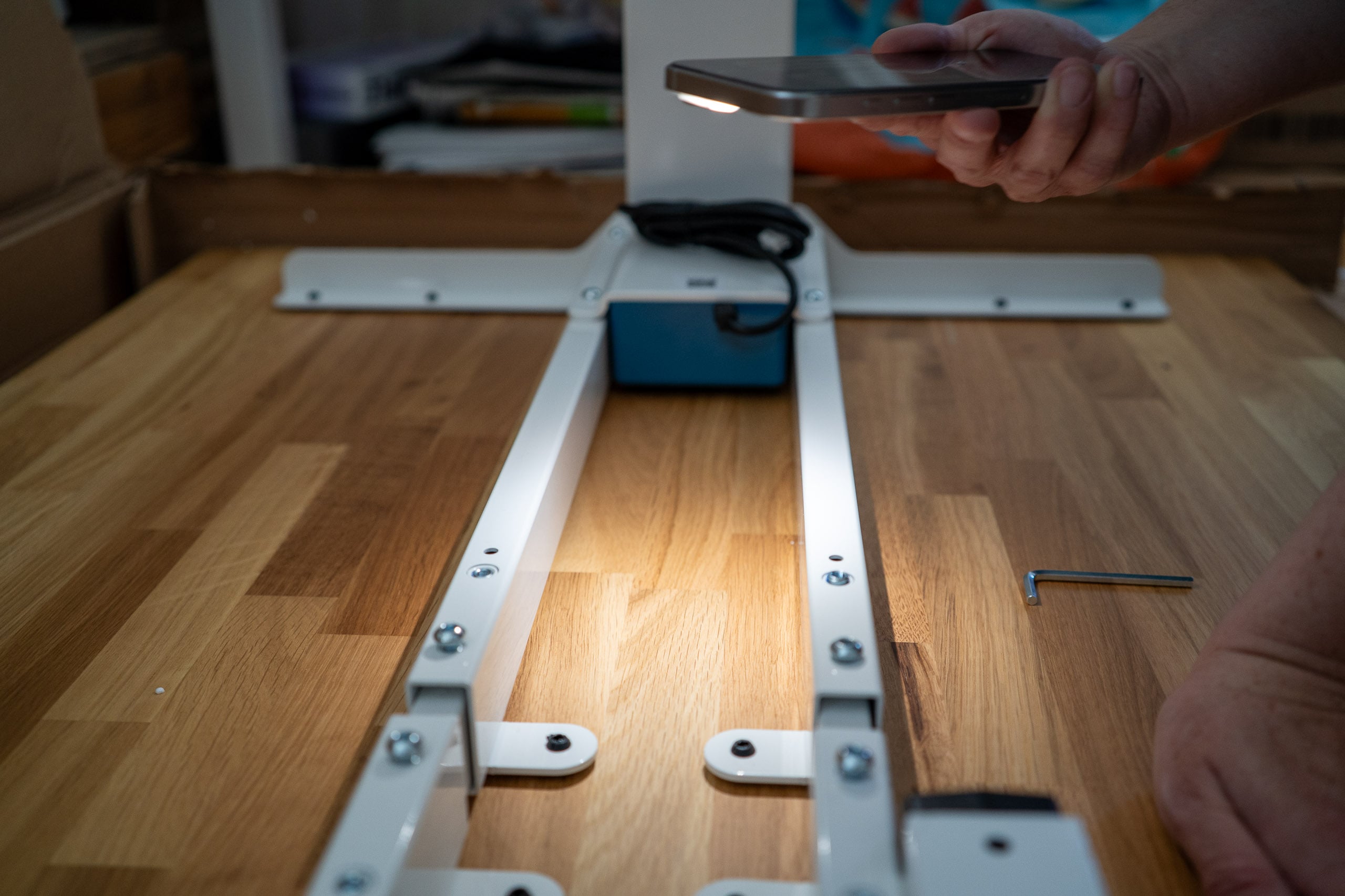 Neid am Arbeitsplatz: der Flexispot E200 im Test Montage des weißen E200-Gestells auf der Unterseite der Eichenplatte, beleuchtet mit Handy-Taschenlampe
