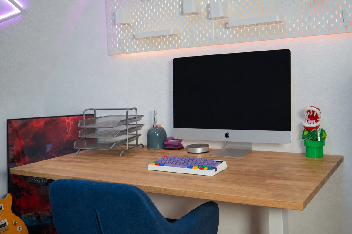 Neid am Arbeitsplatz: der Flexispot E200 im Test Fertig aufgebauter Flexispot E200 mit iMac und bunter Tastatur, dahinter beleuchtete SKÅDIS-Wand