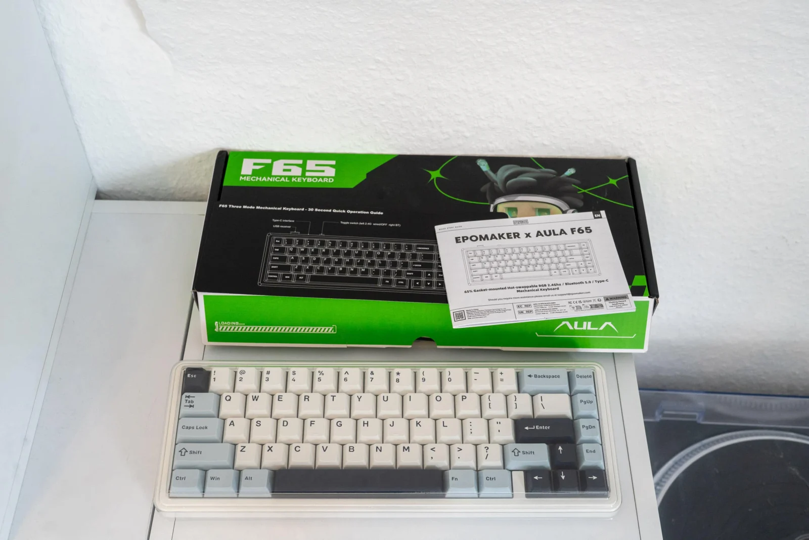 Günstig, gasket, geil? Was die EPOMAKER x AULA F65 wirklich kann F65 mechanische Tastatur mit weißen Tasten und schwarzer Tastaturbelegung, Verpackung im Hintergrund.