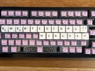 Edelstahl-Tastatur mit pinken Custom-Keycaps und weißen Tastenkappen in deutscher Layout.