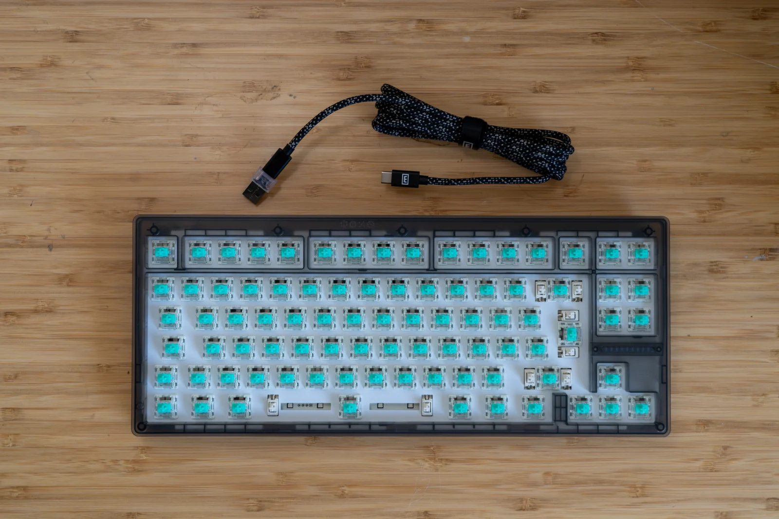 Wooting 80HE Test: Hall-Effect trifft Rapid Trigger – Gaming und Custom vereint? Hell erleuchtete mechanische Tastatur ohne Keycaps auf Holz-Oberschicht, mit USB-Kabel.