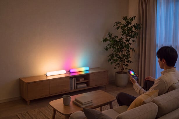 SwitchBot Lightbar: zwei Leisten liegen auf einem Lowboard im Wohnzimmer, ein Mann stellt die Farbe per App ein (Bild: SwitchBot)