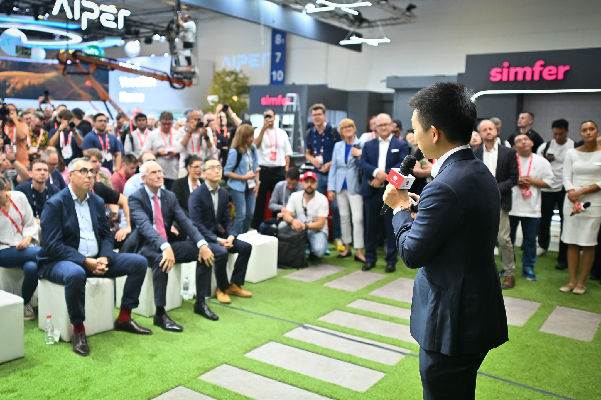 Mähroboter mit Arm: Sechs Hersteller lösen die Rasenkante, und der Igelschutz kostet extra Roborock-Pressetermin auf Kunstrasen auf der IFA 2026, davor sitzt und steht die Presse