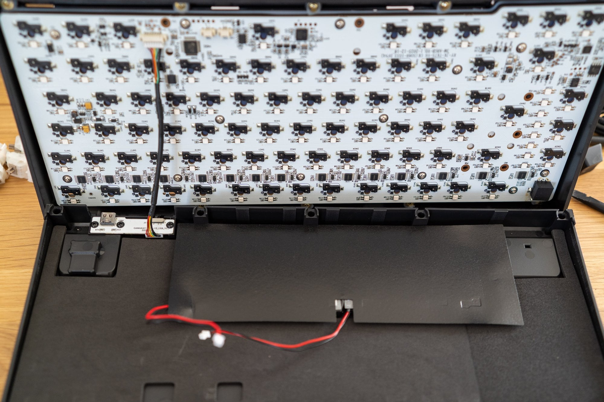 Geöffnete Gamakay TK75 TMR: Platte und Platine hängen am Gehäusedeckel, im Boden liegen nur Akku und USB-Platine, links das Dongle-Fach
