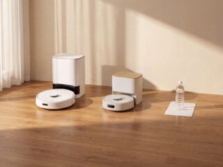 SwitchBot K11+ Pro mit kompakter Absaugstation neben einer größeren Station, daneben DIN-A4-Blatt und 500-ml-Flasche als Größenvergleich (Bild: SwitchBot)