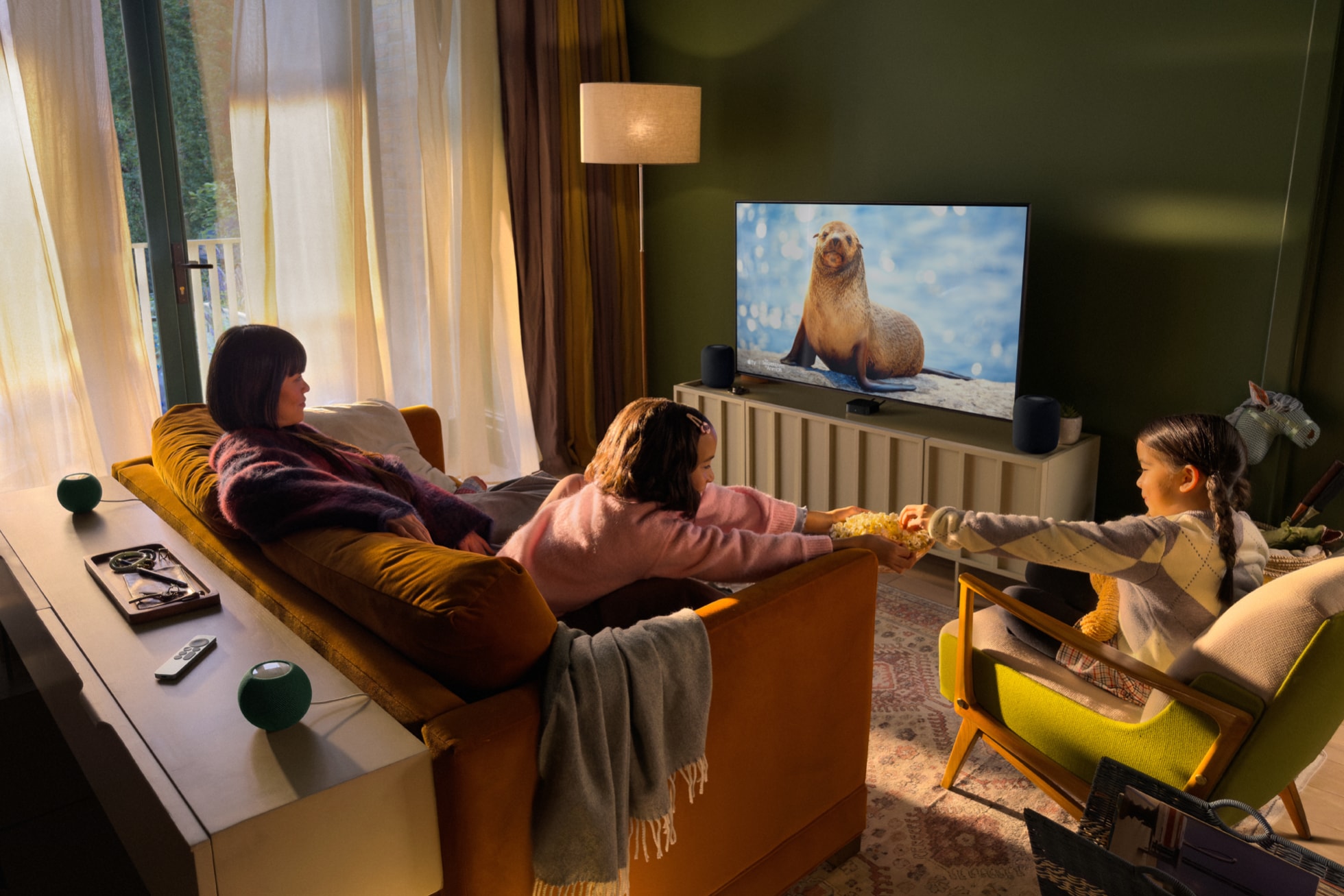 Wohnzimmer mit Apple TV 4K am Fernseher und vier HomePod mini 2 als Surround-Lautsprecher vorne und hinten