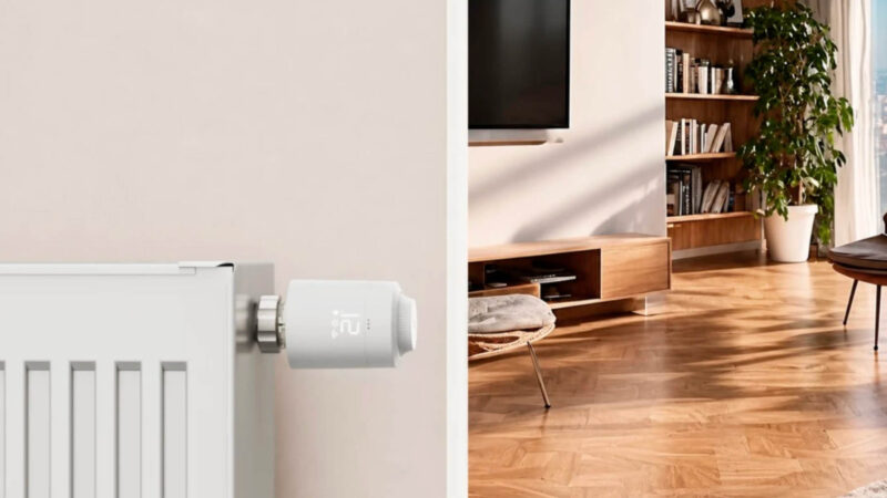 Hama Heizkörperthermostat mit Matter over Thread an einem weißen Heizkörper, dahinter ein Wohnzimmer mit Holzboden