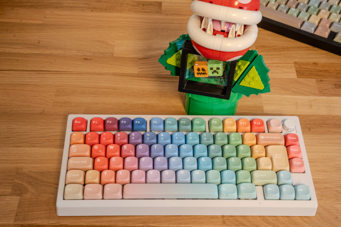 SIMPOCUBIC Rhapsody MOA Keycaps komplett auf der weißen Zoom75, Regenbogen-Verlauf, ISO-DE mit Umlauten, dahinter die Lego-Piranha-Pflanze