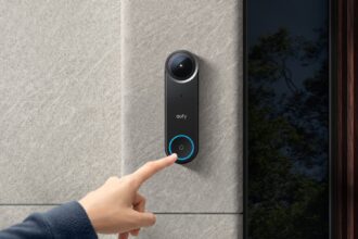 eufy Video-Türklingel S4 an einer Steinwand neben der Haustür, ein Finger drückt den beleuchteten Klingelknopf