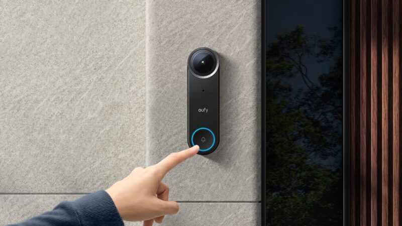 eufy Video-Türklingel S4 an einer Steinwand neben der Haustür, ein Finger drückt den beleuchteten Klingelknopf